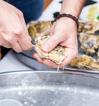 man opent oester met mes