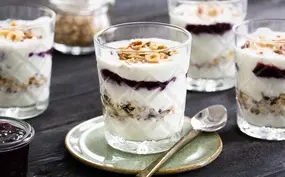 Feestelijke ontbijttrifle met laagjes jam, knapperige noten, voedzame muesli en yoghurt (of kwark). 