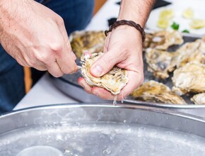 man opent oester met mes